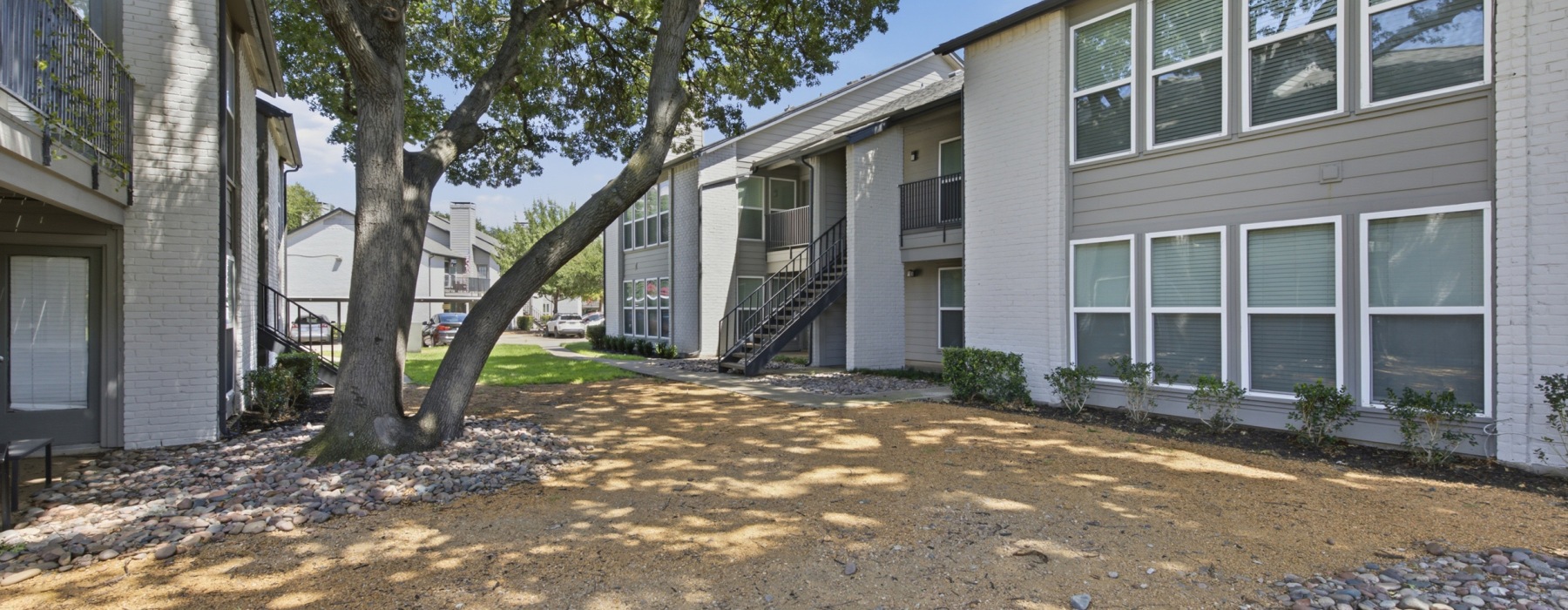 Exterior view of multi-story apartment buildings with private balconies and mature shade trees at Communities of Bent Tree