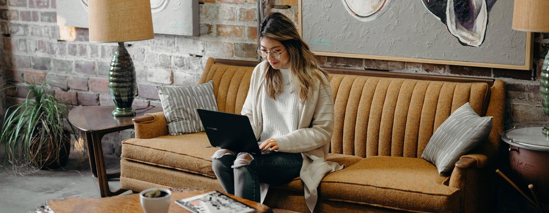 a woman sitting on a couch working on a laptop