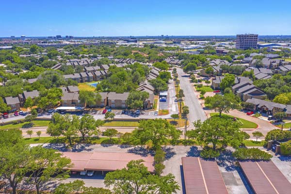 Drone shot looking down Ledgemont Lane in Addison TX where the apartment community resides. Bent Tree Fountains on the left side of the road and Bent Tree Brook is on the right side.