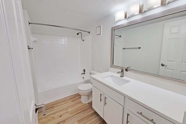 Secondary bathroom with custom mirror frame, quartz countertops, refinished cabinetry, and brushed nickle fixtures.